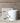 White mug with text and design on a wooden surface with a box and flowers.